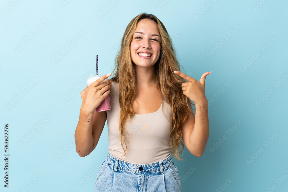 Young woman with strawberry milkshake isolated on blue background giving a thumbs up gesture Young woman with strawberry milkshake isolated on blue background giving a thumbs up gesture
