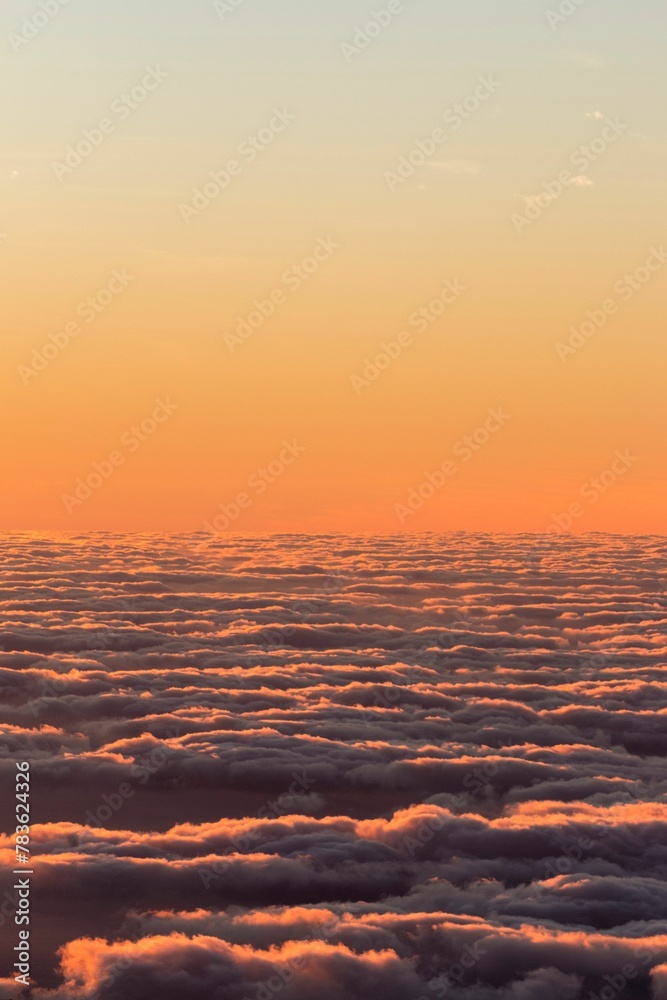 Obraz premium Vertical shot of the colorful and half-cloudy sunset with the view over the clouds