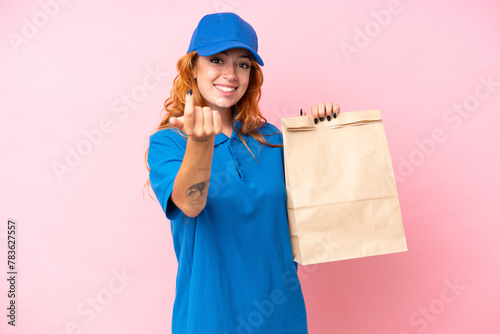 Young caucasian woman taking a bag of takeaway food isolated on pink background doing coming gesture