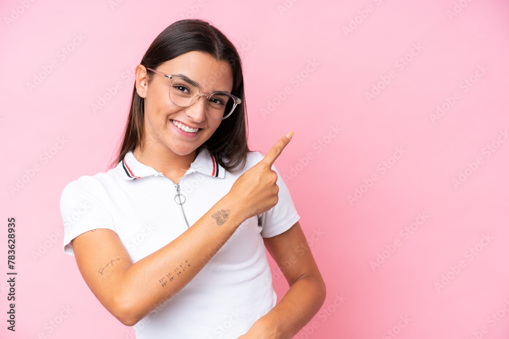 Young caucasian woman isolated on pink background With glasses and pointing side