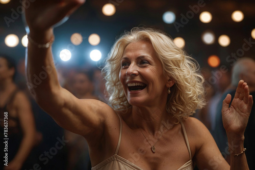 A happy senior aged woman dancing in a club, enjoying herself as she tries to follow and learn a dance routine. Beautiful old lady dancing with the crowds, living a physical and socially active life.