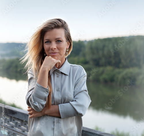 Portrait of a beautiful smiling woman in a gray shirt against the background of a river