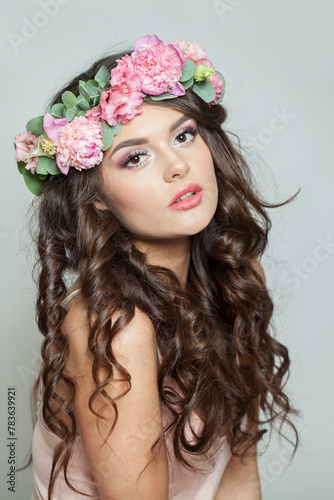 Glamorous female model in floral summer wreath on her hair. Young woman with clean skin and wavy hairstyle on white background