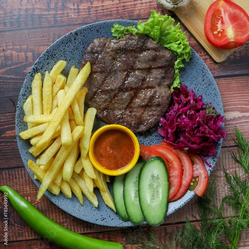 Top view of a plate contains beef burger, French fries, red sauce and vegetables