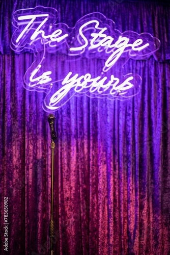 Microphone on a stage with glowing neon writing behind it saying 