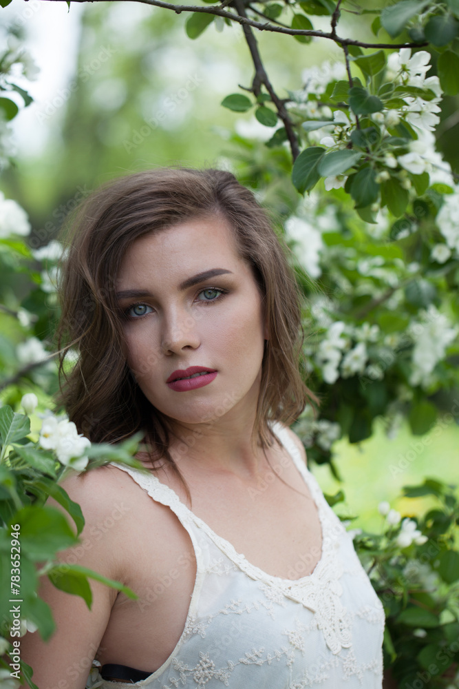 Nice young adult brunette female model with fresh clean skin, bob haircut and natural makeup against green blurred leaves background with white spring flower Nice young adult brunette female model with fresh clean skin, bob haircut and natural makeup against green blurred leaves background with white spring flower