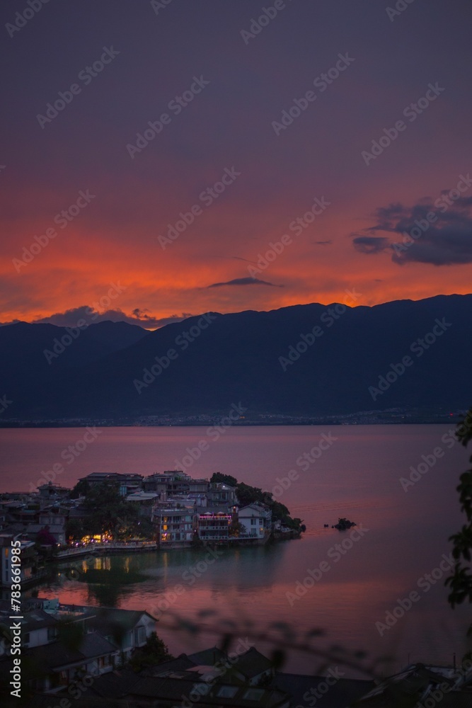 Vertical shot of coastal buildings separated by waters with hills and orange sunset in background Vertical shot of coastal buildings separated by waters with hills and orange sunset in background