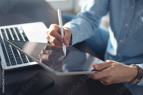 Young casual business woman sitting on the floor using stylus pen and digital tablet, working on laptop computer at home office. Female student online studying, E-learning