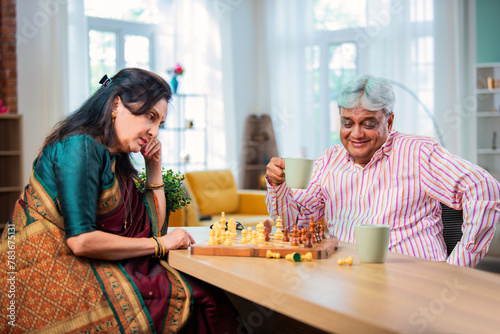 Mature Indian couple enjoying while playing chess board game together at home. photo