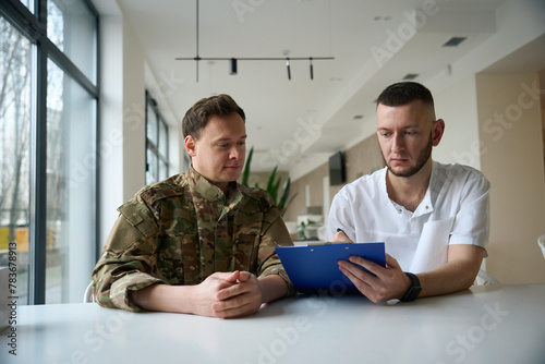 Healthcare professional is making notes in presence of enlisted man