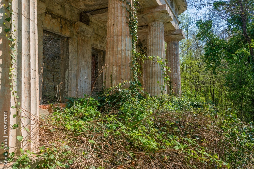 colonnade of an old abandoned dilapidated villa surrounded by the first spring bright green foliage in an abandoned park on the Black Sea coast on a sunny day in April