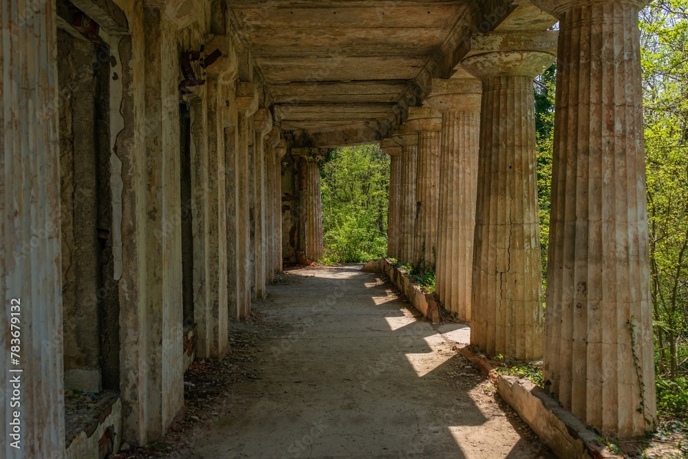 colonnade of an old villa in ancient Greek style surrounded by thickets of trees with young bright green foliage on a sunny spring day