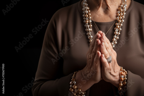 Mature woman's hands in prayer position with black background and copy space