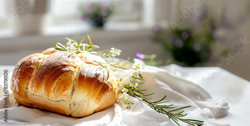 A delicious looking French rosemary bun lies on a white linen tablecloth. Natural light from the window illuminates the scene