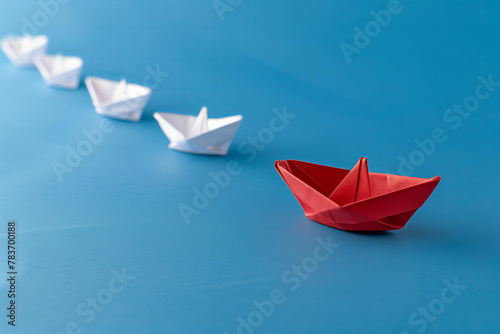 red paper boat leading other white boats on a blue background, symbolizing leader focus and strategic direction. photo