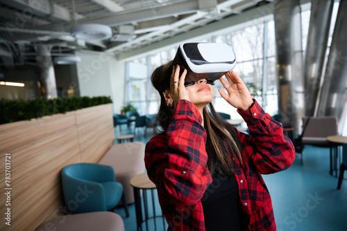 Young focused female IT manager using VR glasses in hall of coworking office