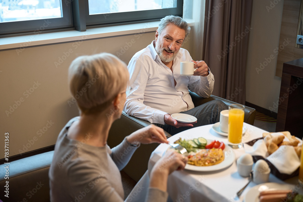 Man with cup of tea or coffee and woman having breakfast looking at each other Man with cup of tea or coffee and woman having breakfast looking at each other