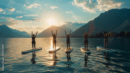 Five adults perform yoga on stand-up paddleboards in a serene lake setting, surrounded by lush mountains and clear waters, demonstrating balance and tranquility. photo
