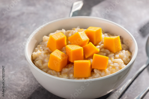 porridge with pumpkin. on a stone table there is a small white plate with rice porridge and orange pumpkin cubes, top view breakfast concept
