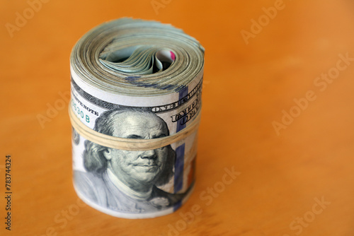 financial image of close up rolled and rubber banded American one hundred dollar bills pile on desk