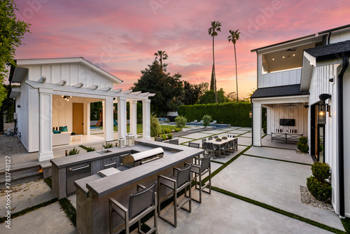 the outdoor kitchen with a fireplace, table and chairs at dusk © Wirestock