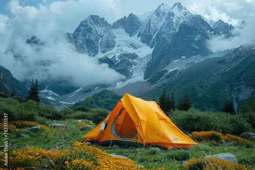 Striking orange camping tent surrounded by wildflowers with snowy mountains under a cloudy sky