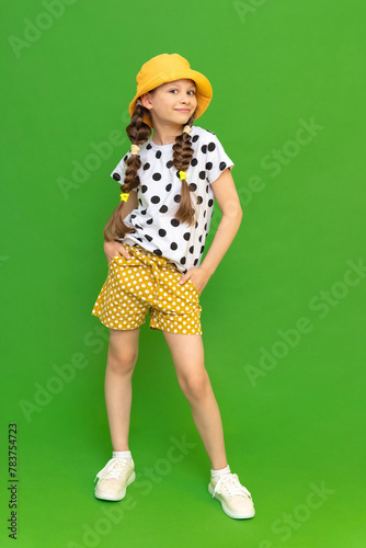 A little girl in a hat and shorts is enjoying the warm summer. Children's summer holidays.  Summer clothes for a child. Green isolated background.