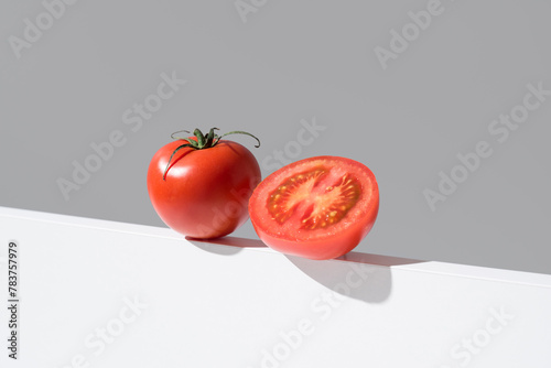 Un tomate maduro entero y cortado por la mitad sobre un soporte blanco y fondo gris photo