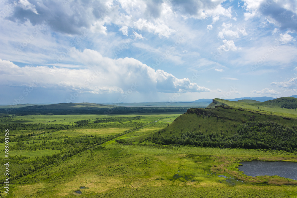 Obraz premium Green hills and a small pond on the background of a blue sky with clouds