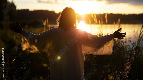 Silhouette of man in tunic stands open hand beside lake praying with sunset in the background  photo