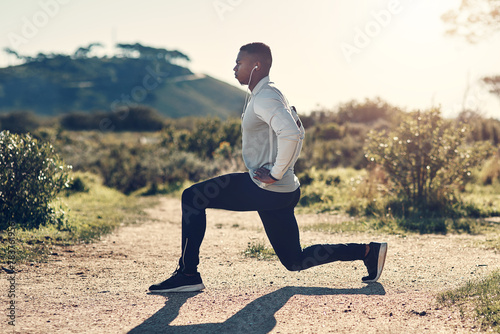 Fitness, stretching and black man in mountain with headphones, health and wellness for outdoor run. Muscle workout, warm up and athlete in nature with music streaming, earphones and exercise on path.