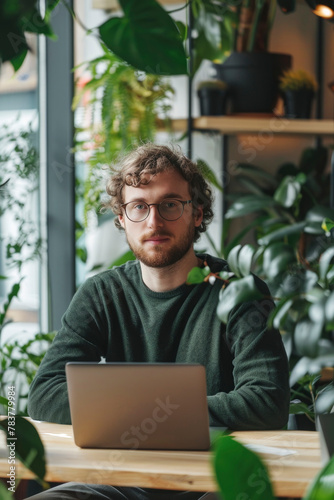 Young Male Freelancer Working on Laptop in Plant-Filled Cafe