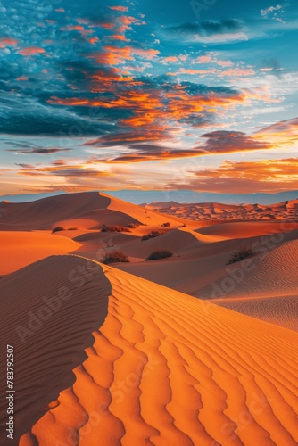 A panorama of a desert landscape at sunset  with rolling sand dunes casting long shadows and the sky ablaze with color