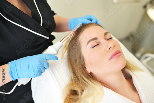 dermatologist trichologist performs the procedure with a darsonval device to improve the condition and quality of the patient's hair.