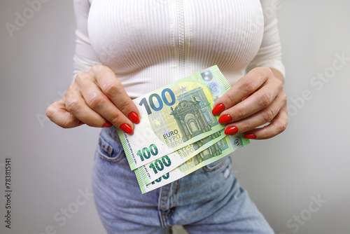 A close-up of a euro bill with a denomination of one hundred which is held by a woman's hands. A girl in jeans with a euro banknote in her hands.