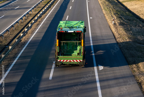 Green Truck for transportation of municipal waste (garbage truck) moves on an empty highway. Urban recycling waste and garbage services. photo