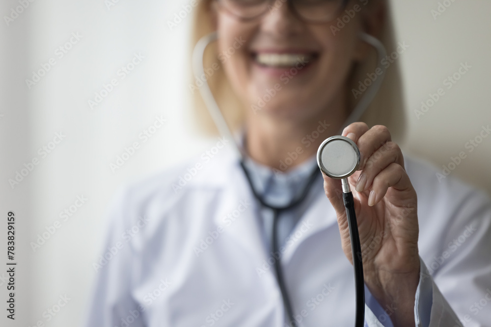 Close up of smiling mature woman cardiologist showing to camera stethoscope. Assessing patient health, listen internal body sounds, check health condition of heart or lungs, measure of blood pressure - obrazy, fototapety, plakaty 