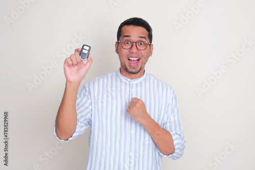 Adult Asian man clenched fist and showing wow face expression while holding a car key photo