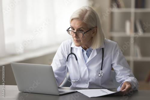 Mature woman therapist working on laptop, sit at desk with papers, prepare treatment plan, check patient medical records, make research and clinical guidelines, reviewing data, do administrative tasks © fizkes