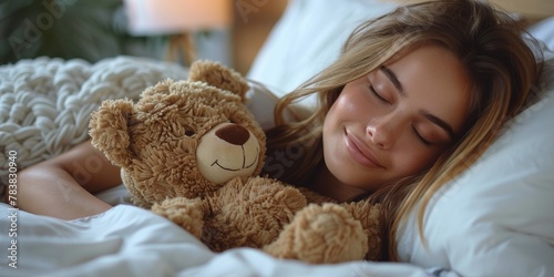 A charming woman smiles peacefully, embracing a teddy bear in a cozy bedroom.