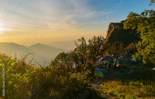 A group of tents are set up on a hillside, with a beautiful sunset in the background. Concept of adventure and relaxation, as people gather in the outdoors to enjoy the natural beauty of the area photo