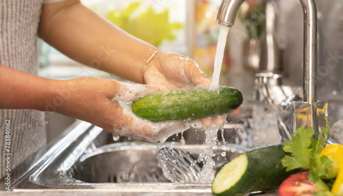 Hands of a homemaker washing cucumbers in the sink of their home. This is done to maintain good food hygiene and take care of their family always. The fruits were purchased at the supermarket







