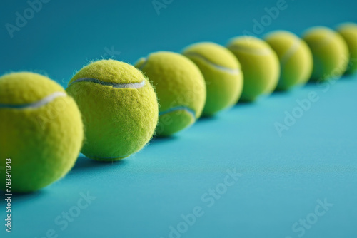 A row of tennis balls arranged neatly on a vibrant blue surface, ready for a game of tennis © SHOTPRIME STUDIO