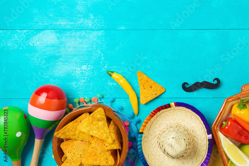 Nacho tortilla chips, peppers, maracas and sombrero hat on blue wooden background. Mexican party Cinco de Mayo holiday celebration. Top view, flat lay
