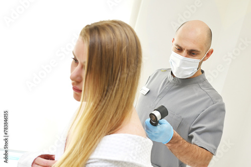 A dermatologist examines neoplasms on the patient's skin using a special dermatoscope device. Prevention of melanoma.
