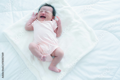 Bild auf Leinwand An infant lying on white bedding is crying, expressing early childhood distress