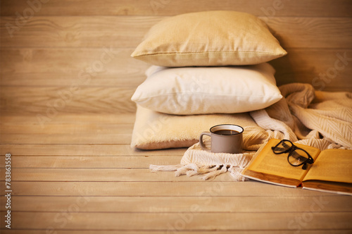 Cup of tasty coffee and glasses on book in composition with plaid and pillows