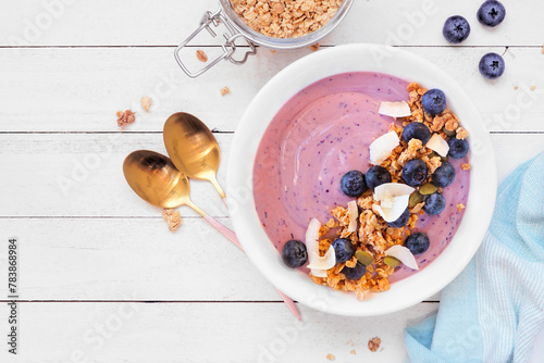 Healthy blueberry and coconut smoothie bowl with granola. Above view table scene on a white wood background.