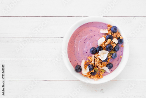 Healthy blueberry and coconut smoothie bowl with granola. Top view on a white wood background.
