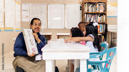 Hispanic adult male teacher holding a book and teach a preschool children.